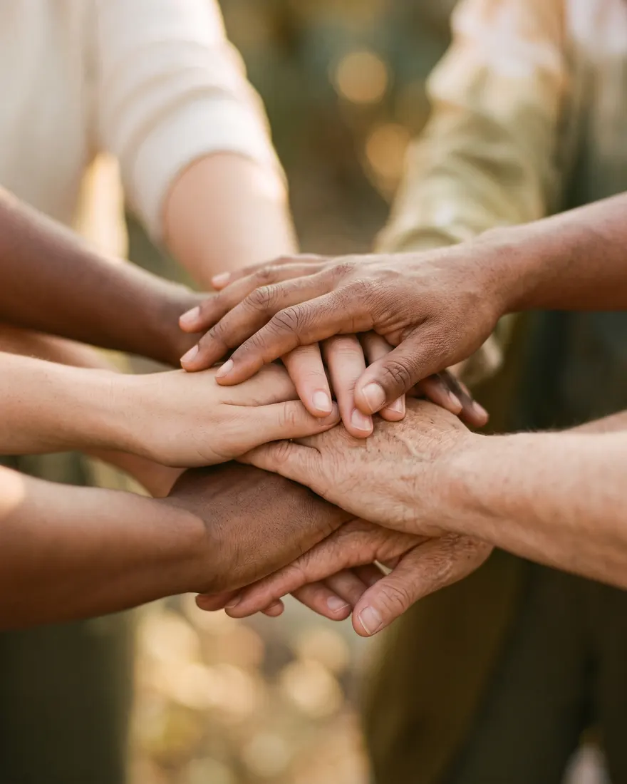Several hands joined together in warm golden light
